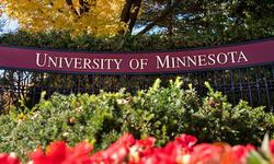 Sign says University of Minnesota with red flowers and a green bush in front